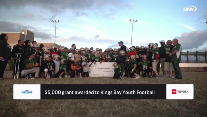 A large group of kids in football gear hold a check from SNY Play Ball donating $5,000 to Kings Bay.