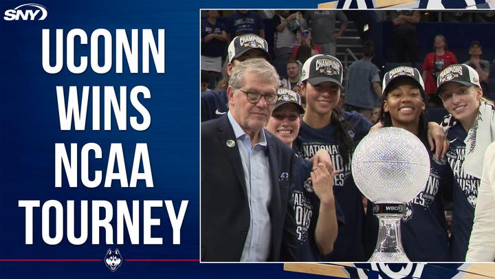 UConn players and coach Auriemma celebrate NCAA Championship win with trophy and smiles.