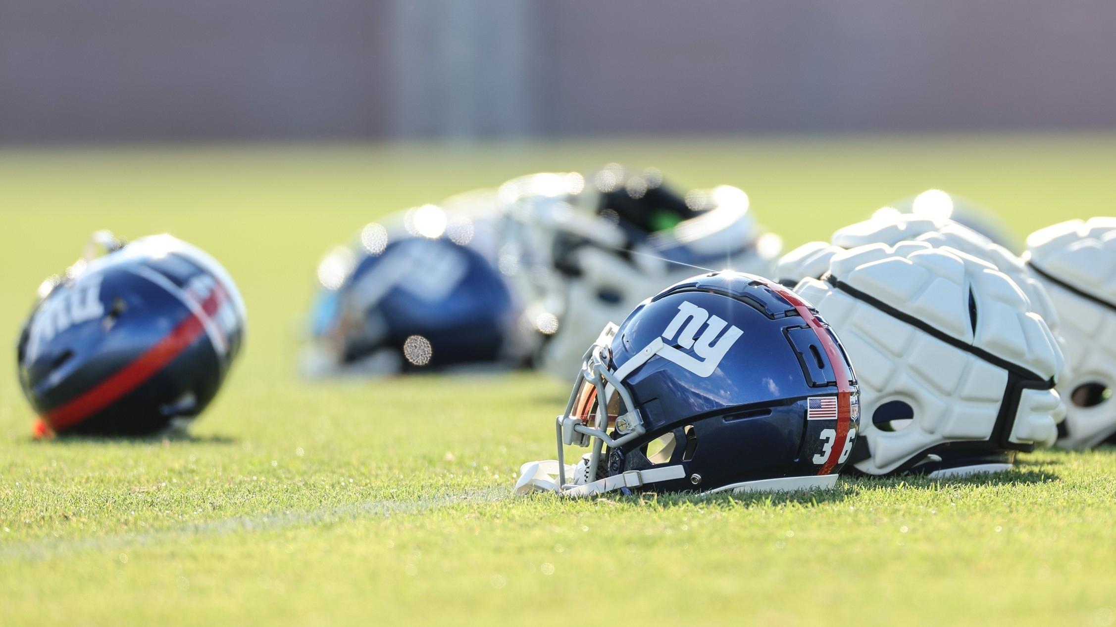 New York Giants helmets rest on the grass field during training camp.